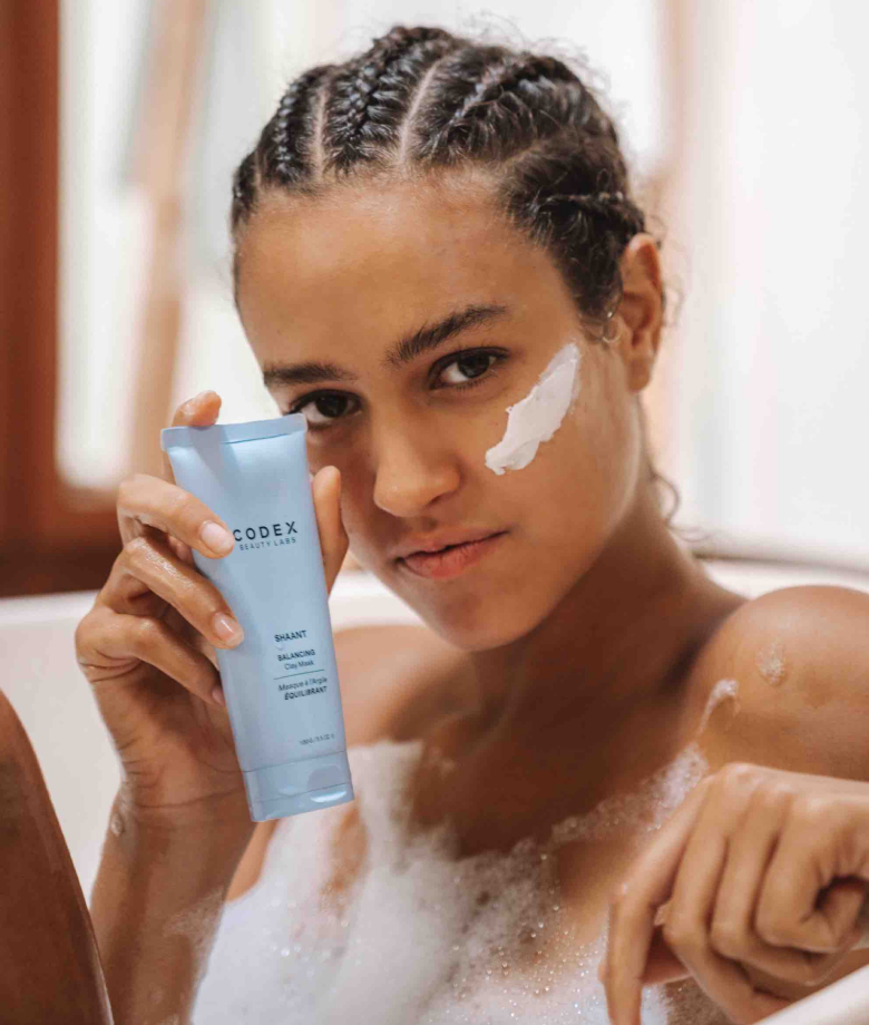Woman holding a bottle of Shaant in a bathtub.